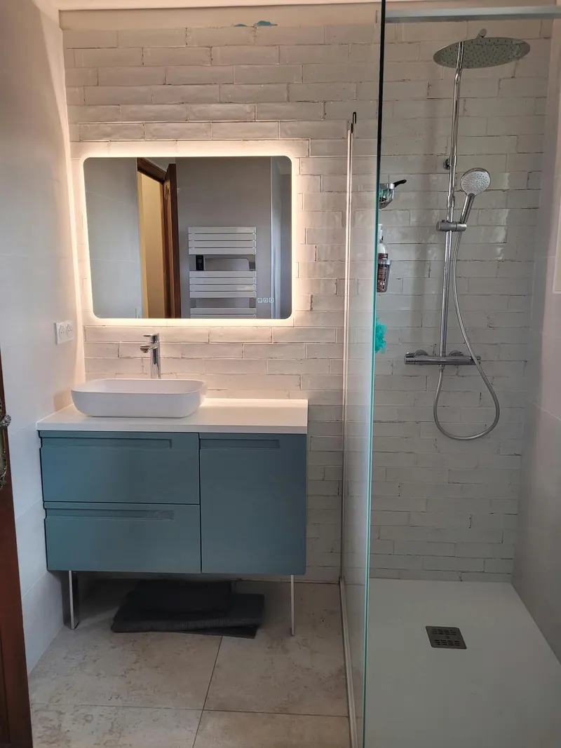 Salle de bain avec meuble vasque bleu-vert, miroir rétroéclairé et douche à l’italienne vitrée